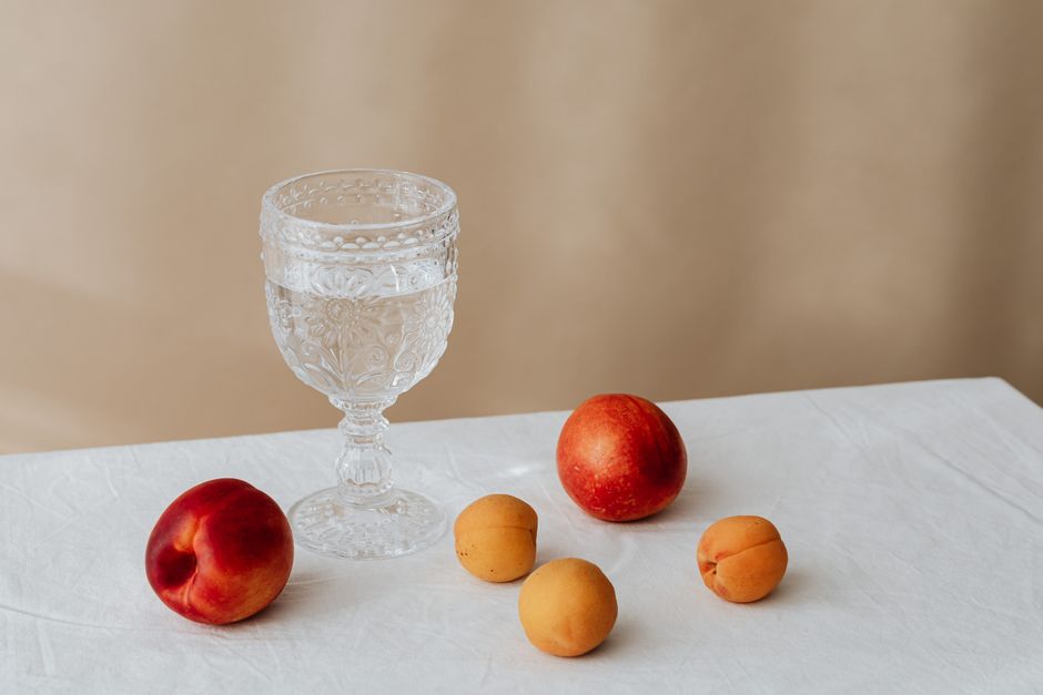Vaso de agua y fruta fresca sobre una mesa de madera junto a una ventana